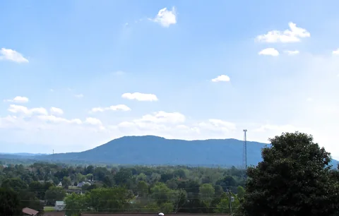 House Mountain rising beyond treetops in Plainview, East Tennessee, under a blue sky with scattered clouds.