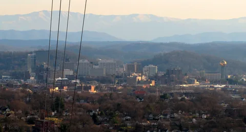Knoxville skyline in the valley below Sharps Ridge, with power lines in front and Smoky Mountain ridges behind.