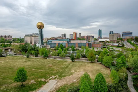 Downtown Knoxville with the golden Sunsphere tower rising above a park lawn and city buildings.