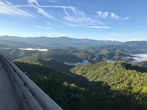 Green Smoky Mountain ridges with fog in the valleys, seen from beside a Foothills Parkway guardrail.