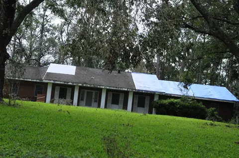 A blue tarp covering storm damage on the roof of a brick ranch house.