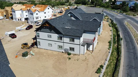 New multifamily building with a dark gray shingle roof, unfinished framed units and a curving road beyond.