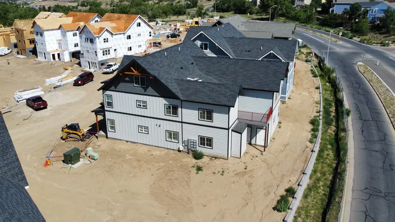 New multifamily building with a dark gray shingle roof, unfinished framed units and a curving road beyond.
