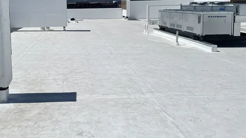 Finished white TPO roof with parapet walls and a large rooftop equipment unit, shot from the roof surface.