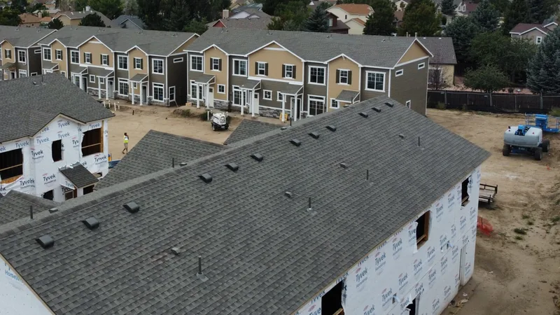 Gray shingles finished on a two-story building in the foreground, house-wrapped units beside it and tan townhomes behind.