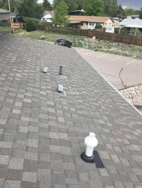 Close-up of a finished gray architectural shingle slope with a white plumbing vent and small roof vents.