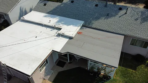 Flat membrane roofs beside a gray shingle slope on a ranch house, seen from above.
