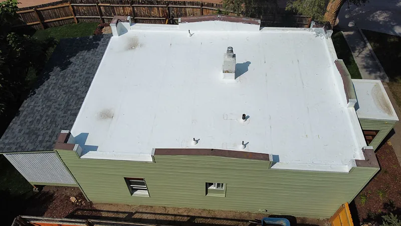 Finished white low-slope roof with a chimney on a green-sided house, a gray shingle slope at left.
