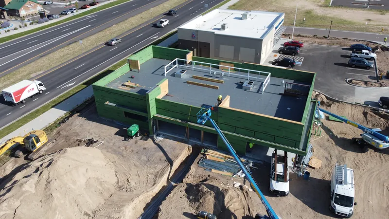 Aerial of a new commercial building with green walls and a membrane roof deck, a boom lift beside it.