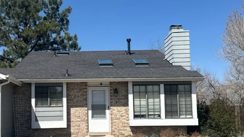 Brick ranch house with a dark shingle roof, two skylights and a tall white chimney chase.