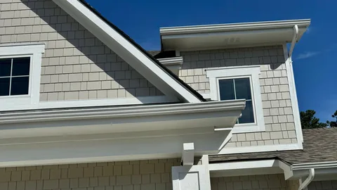 Tan shake siding, white trim boards and white gutters along the eaves of a two-story house.