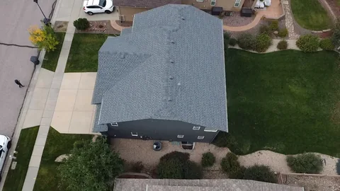 Overhead view of a gray shingle roof on a dark-sided house beside a green lawn and driveway.