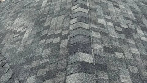 Close view of gray and charcoal architectural shingles meeting at a raised ridge cap.