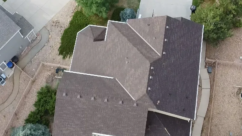 Overhead view of a brown shingle roof with several hips, valleys and vents above a gravel yard.