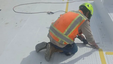 Worker in a hard hat and safety vest fastening a walkway pad on a white membrane roof.