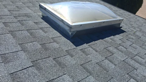 Clear dome skylight on a metal curb set into gray architectural shingles.