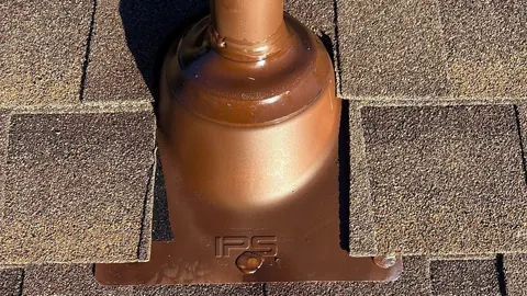 Copper-tone pipe boot flashing set into brown architectural shingles around a vent pipe.